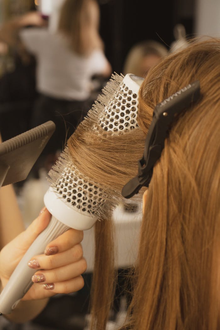 Detailed view of hairstylist curling hair in salon using a round brush and hairdryer.
